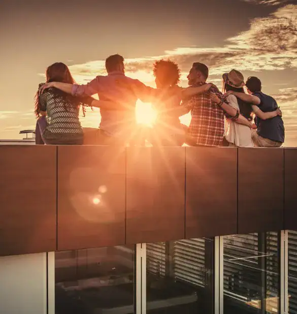 rear view of embraced friends relaxing on a rooftop at sunset